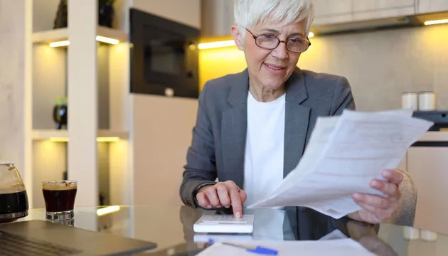 Photo of a woman at a table, holding papers, and using a calculator.